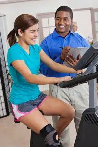Physical therapist helping teen patient with therapy on exercise bike