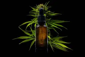 Glass bottle with dispenser with THC oil in front of flowering marijuana plant